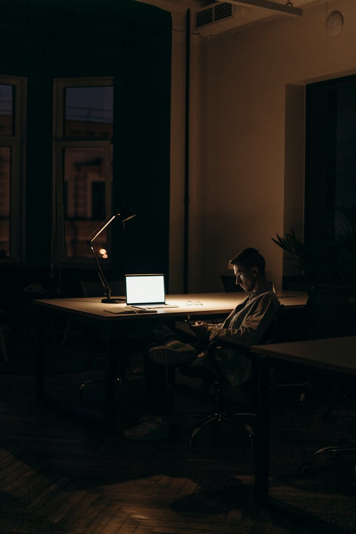 gallery-03 A lone man working on a laptop under dim lighting in a quiet office at night.